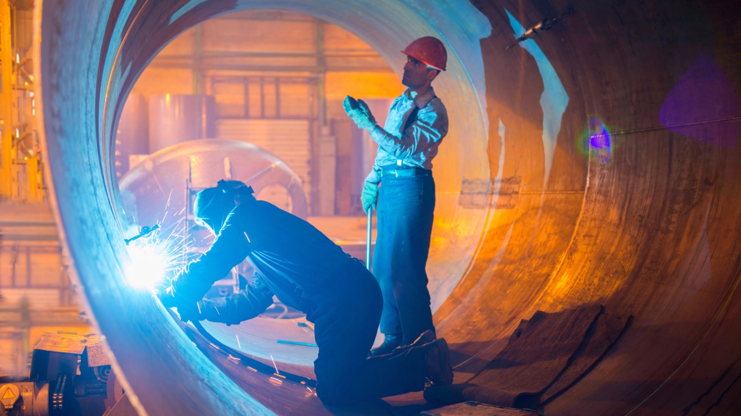 Two male welders working on metal pipe Two male welders working on metal pipe